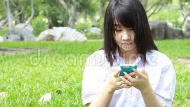 泰国学生十几岁的漂亮女孩用她的智能手机<strong>坐在公园里</strong>。